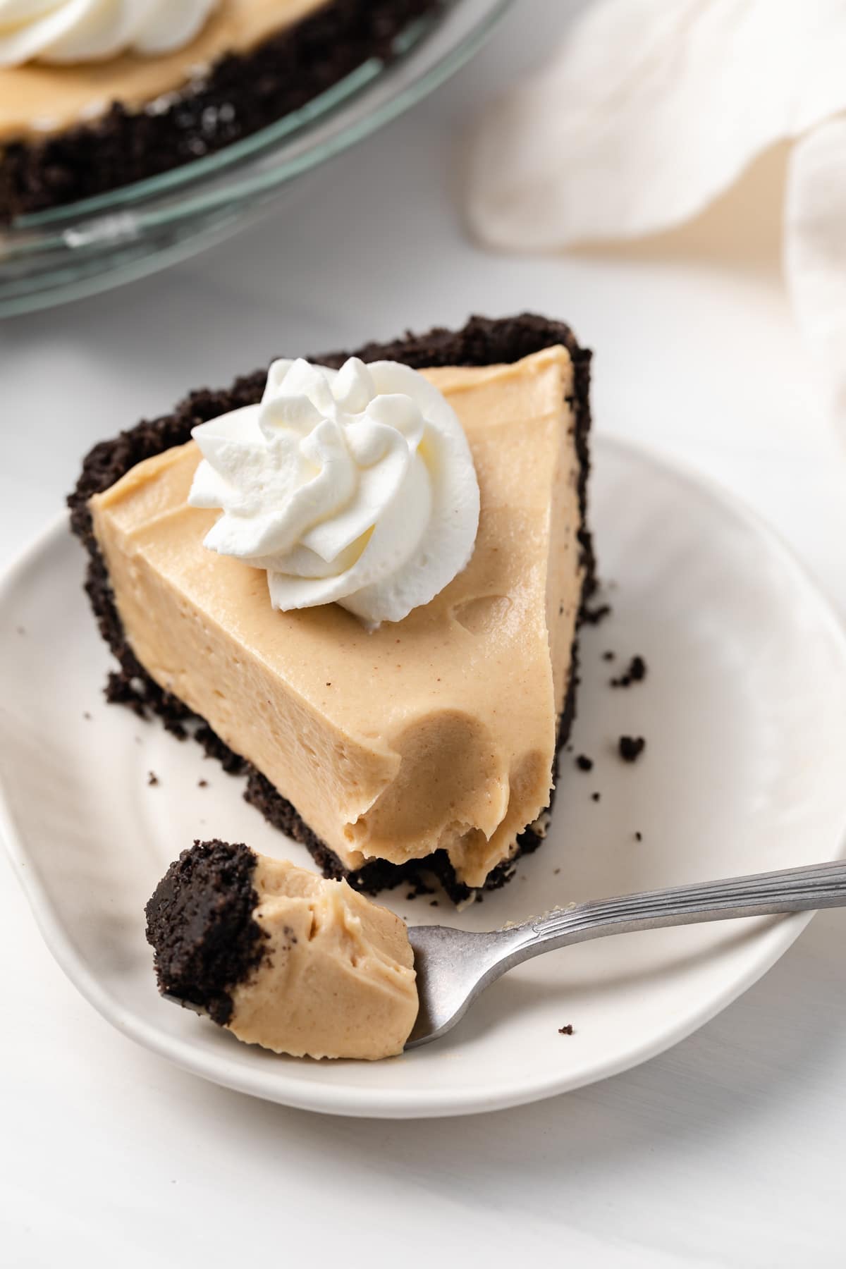 angled view of creamy peanut butter pie topped with whipped cream on a white plate with fork taking a bite out