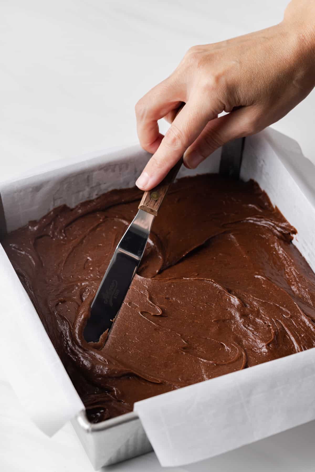 A knife smoothing brownie batter in a pan