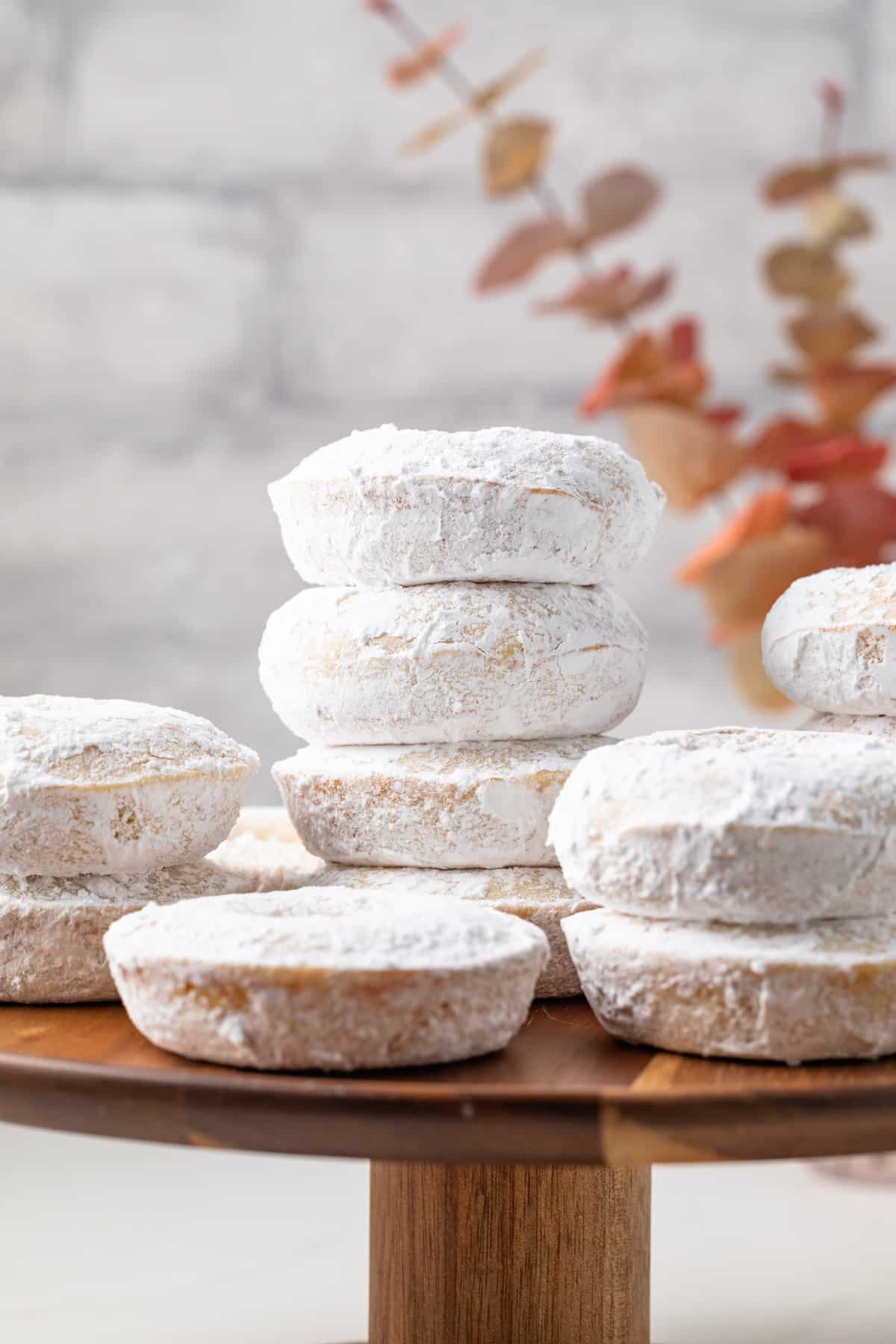 Powdered sugar donuts on a wooden cake stand.