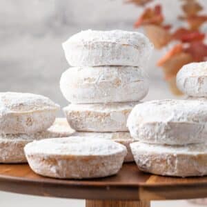 Powdered sugar donuts on a wooden cake stand.