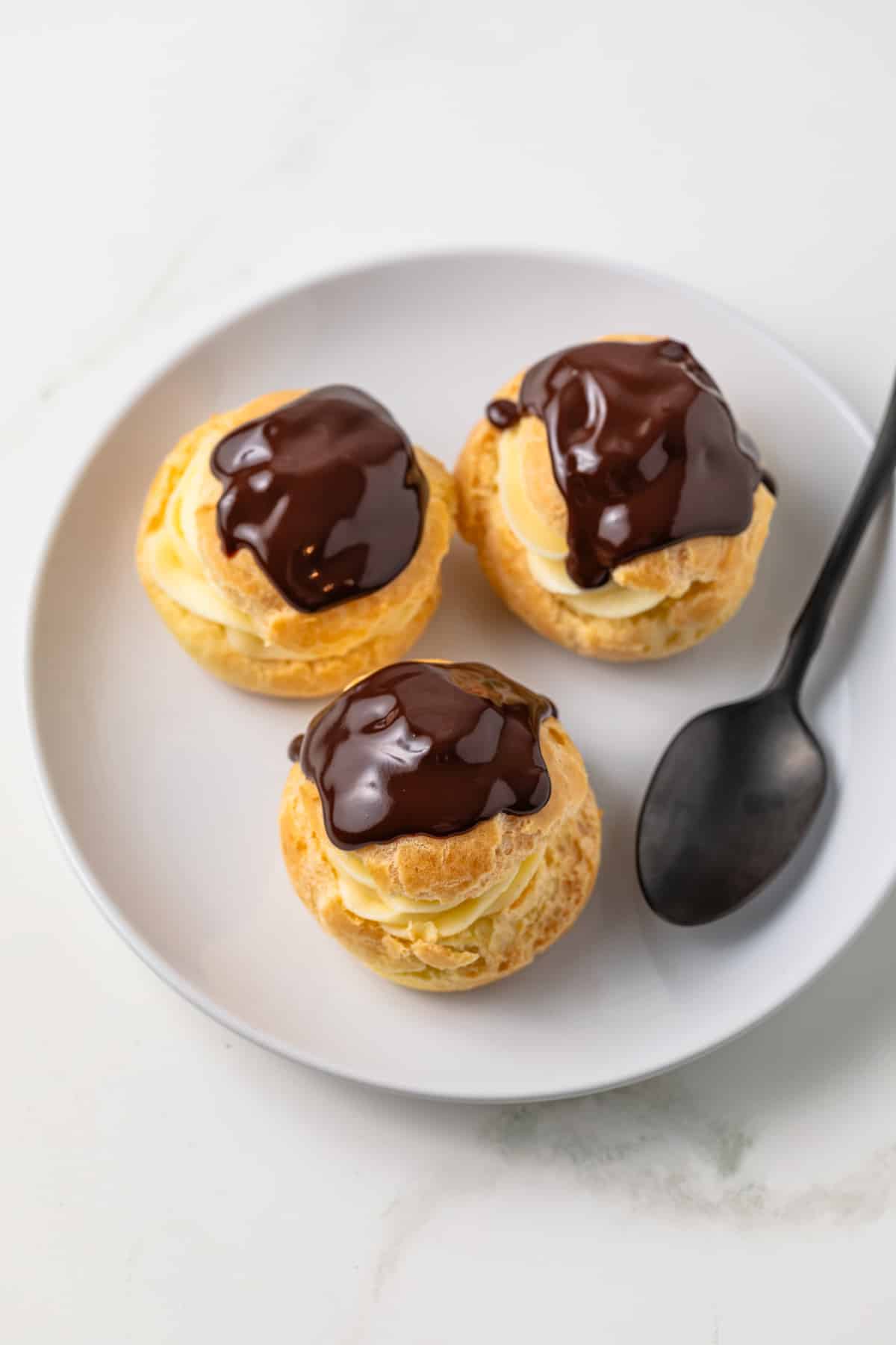 Three profiteroles on a white plate.