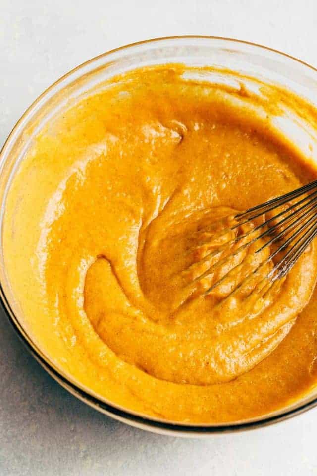 Pumpkin bundt cake batter in a glass bowl with a wire whisk set inside the bowl.