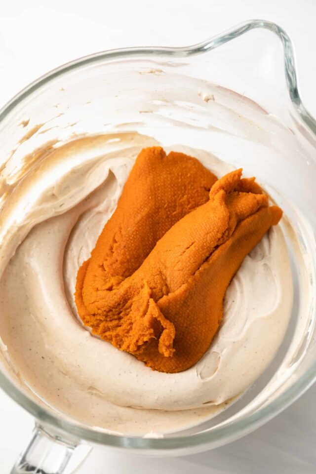 Pumpkin puree being added to cheesecake filling in a mixing bowl
