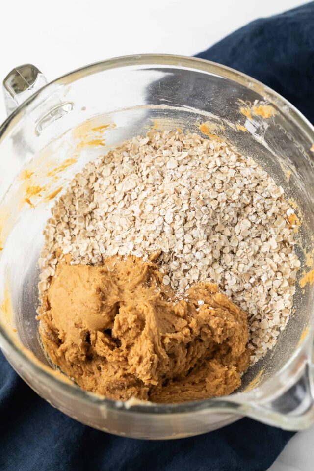 Dry oatmeal on top of raw pumpkin cookie dough in glass bowl