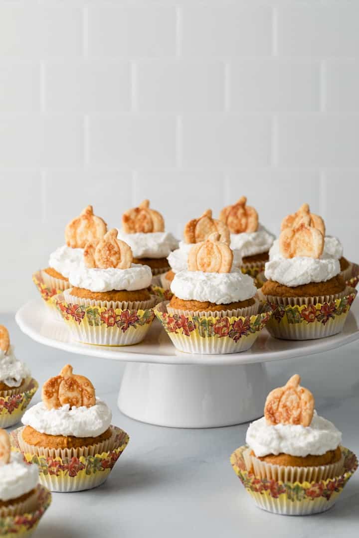 Pumpkin cupcakes with whipped cream frosting and pie crust cutouts on a white cake stand