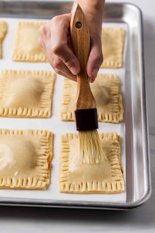 Egg wash being spread on Pumpkin pie pop tarts