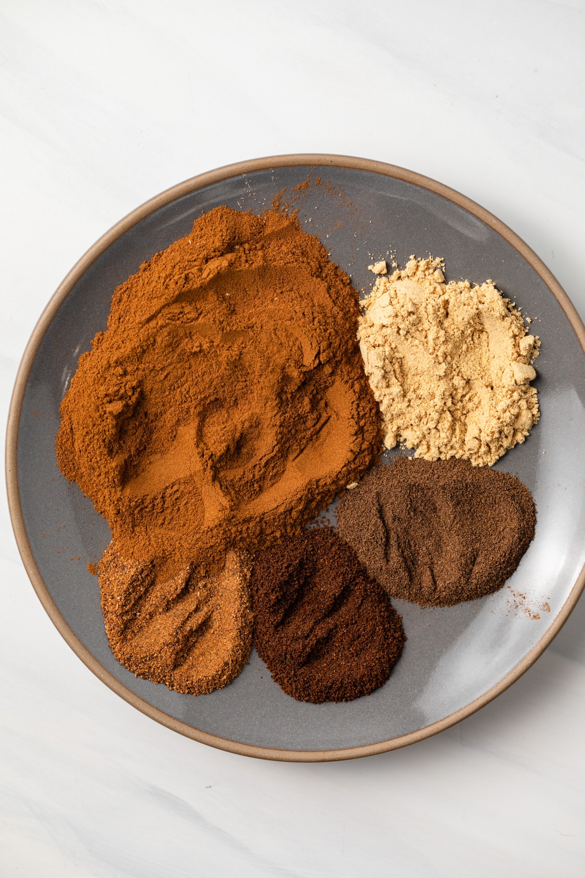Spices for pumpkin pie spice on a plate.
