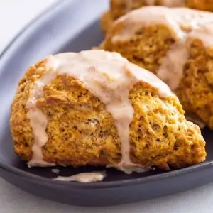side view of pumpkin scones topped with spiced glaze on a dark blue plate
