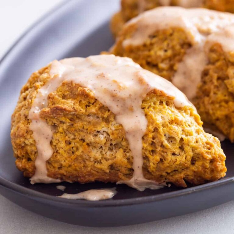 side view of pumpkin scones topped with spiced glaze on a dark blue plate