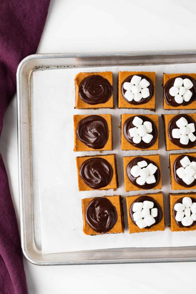 Overhead view of pumpkin bars on a baking sheet topped with chocolate ganache and mini marshmallows