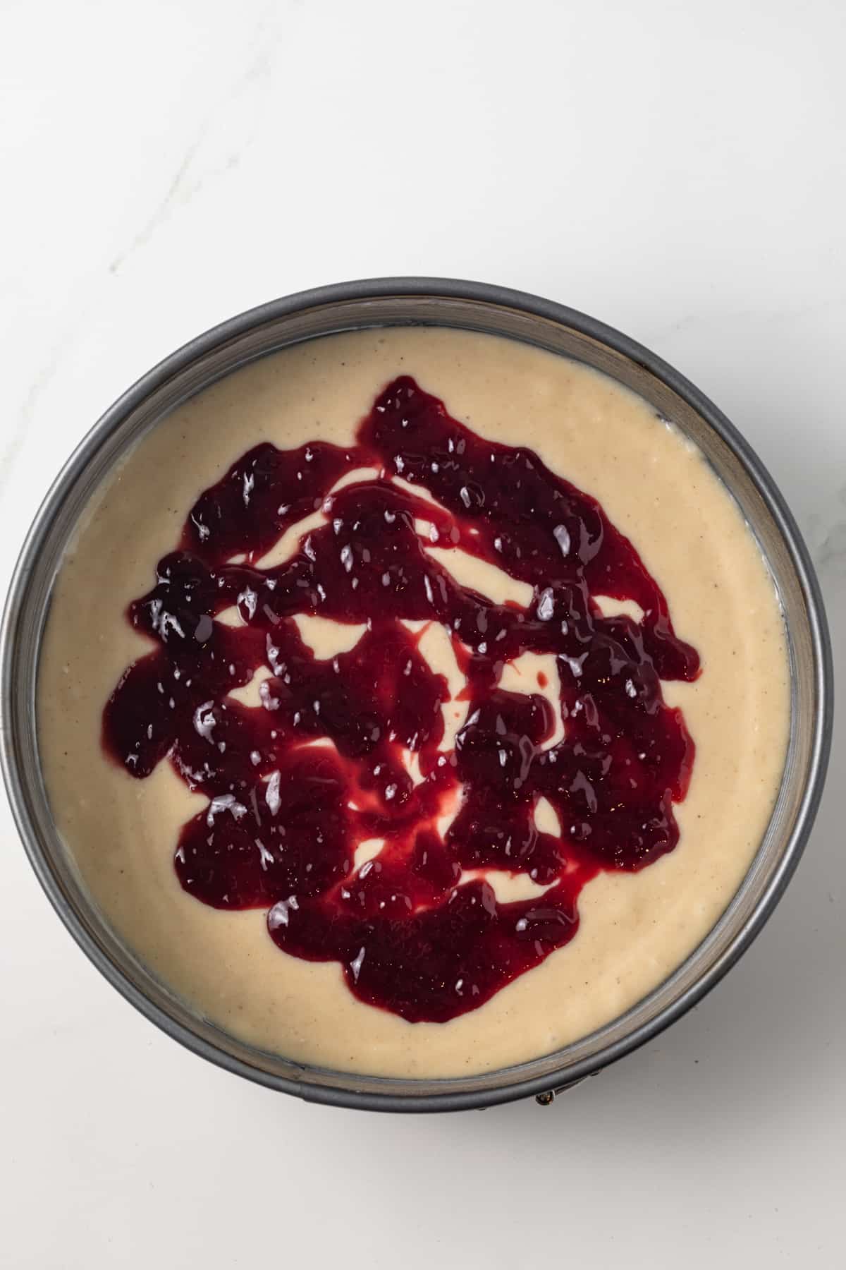 Raspberry jam over cake batter in pan.
