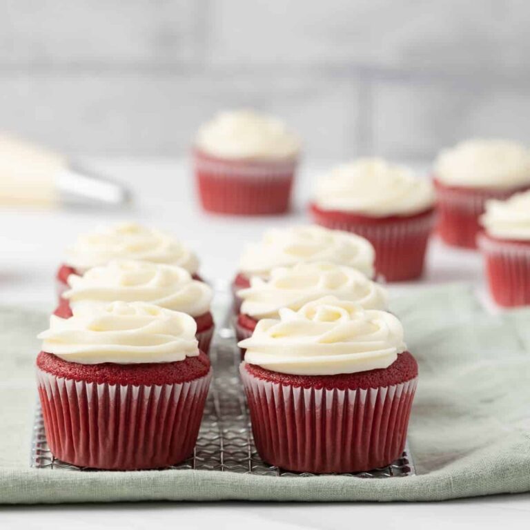 red velvet cupcakes with cream cheese on a wire rack with a green napkin underneath