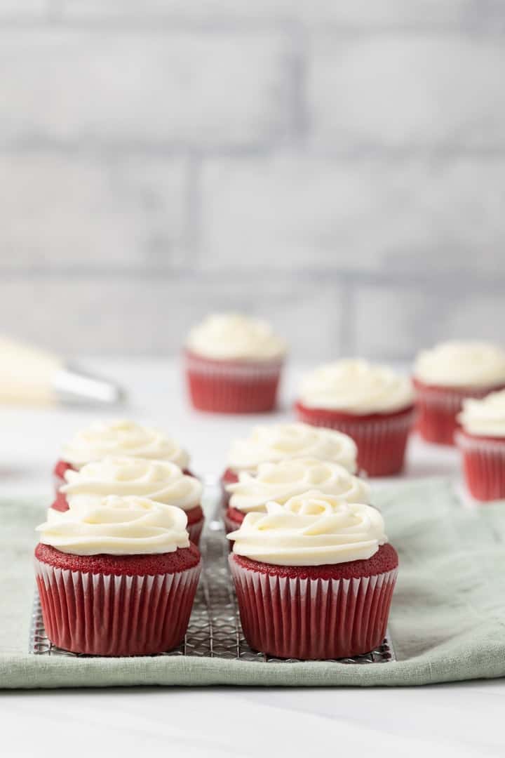 red velvet cupcakes with cream cheese on a wire rack with a green napkin underneath