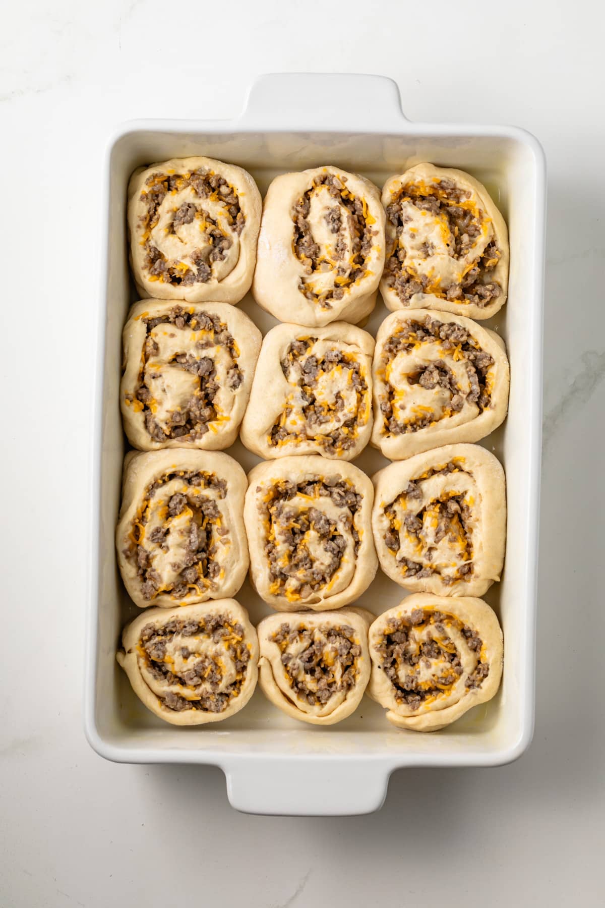 Unbaked sauce and cheese breakfast rolls in pan.
