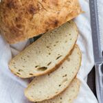 Homemade Slow Cooker Bread sliced on a white towel next to a knife.