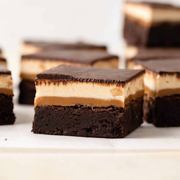 Side view of snickers brownie with fudgy brownie base, gooey caramel, soft peanut butter nougat, and a layer of chocolate