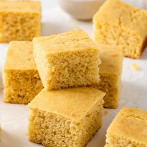 southern cornbread squares stacked on a white background with bowl of butter behind