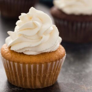 whipped cream swirled over a vanilla cupcake with chocolate cupcakes in the background