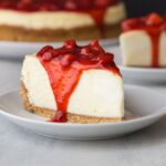 Side view of slice of strawberry cheesecake on white plate.