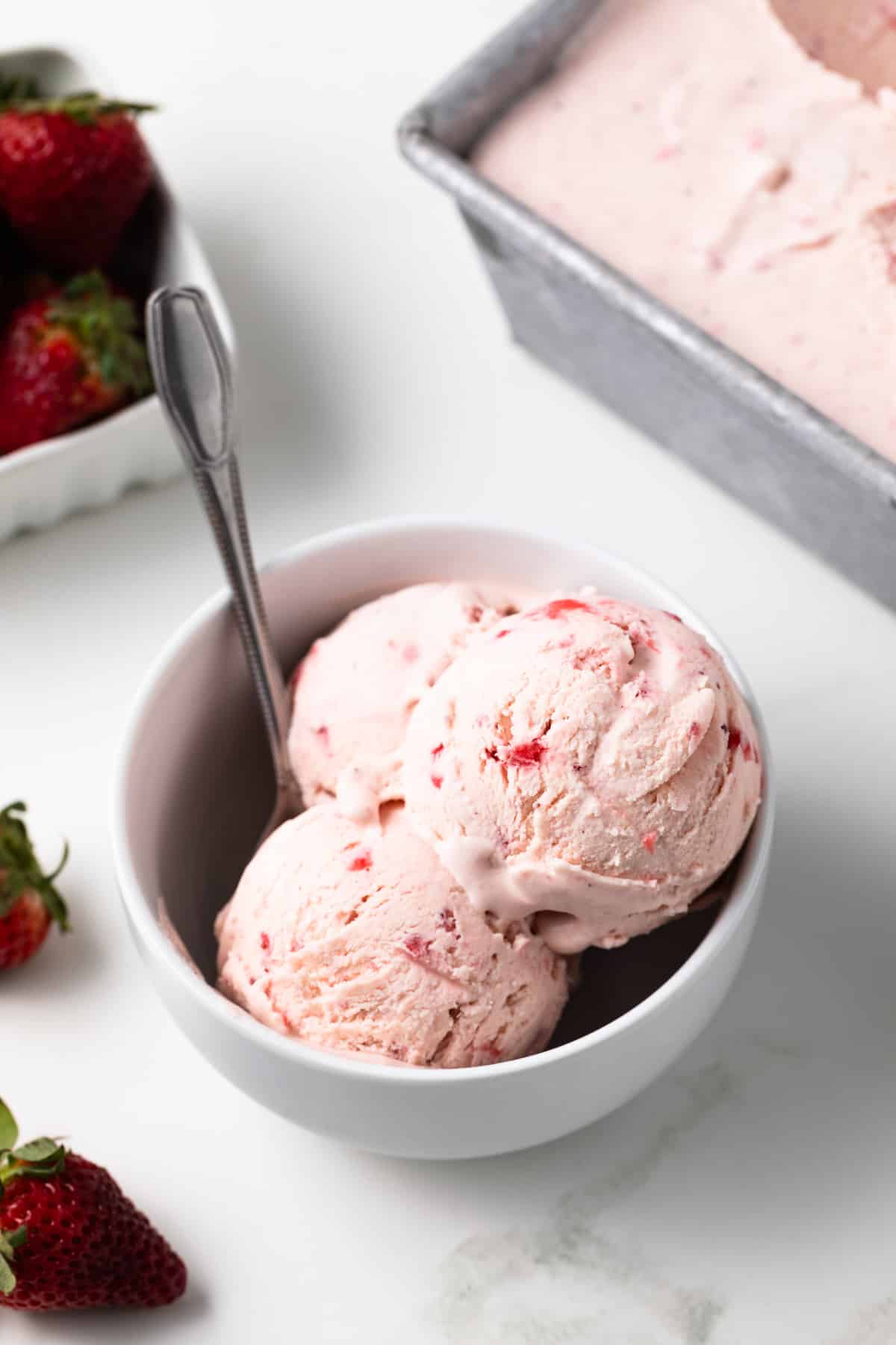 Strawberry ice cream in a bowl with a spoon.