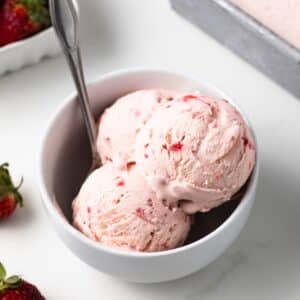 Strawberry ice cream in a bowl with a spoon.