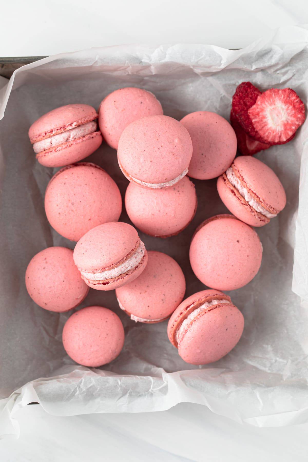 overhead of strawberry French macarons scattered in a square baking pan