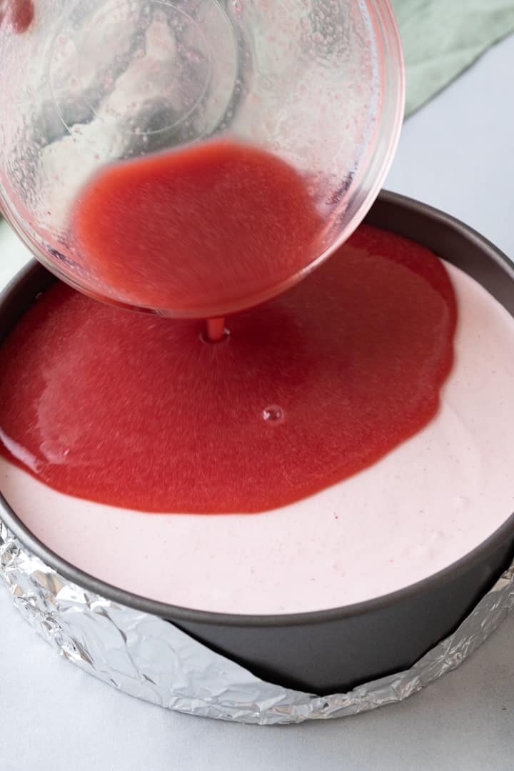 strawberry jam layer being poured over strawberry mousse in a round pan
