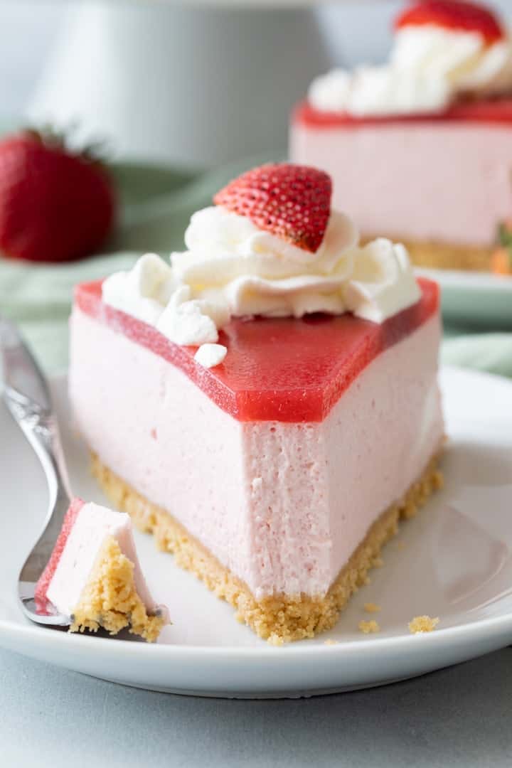 front of a slice of strawberry mousse cake with a fork taking a bite out