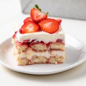 Side view of slice of strawberry tiramisu on white plate.