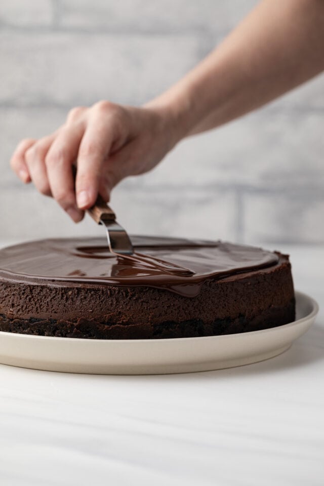 Spreading chocolate ganache over chocolate cheesecake.