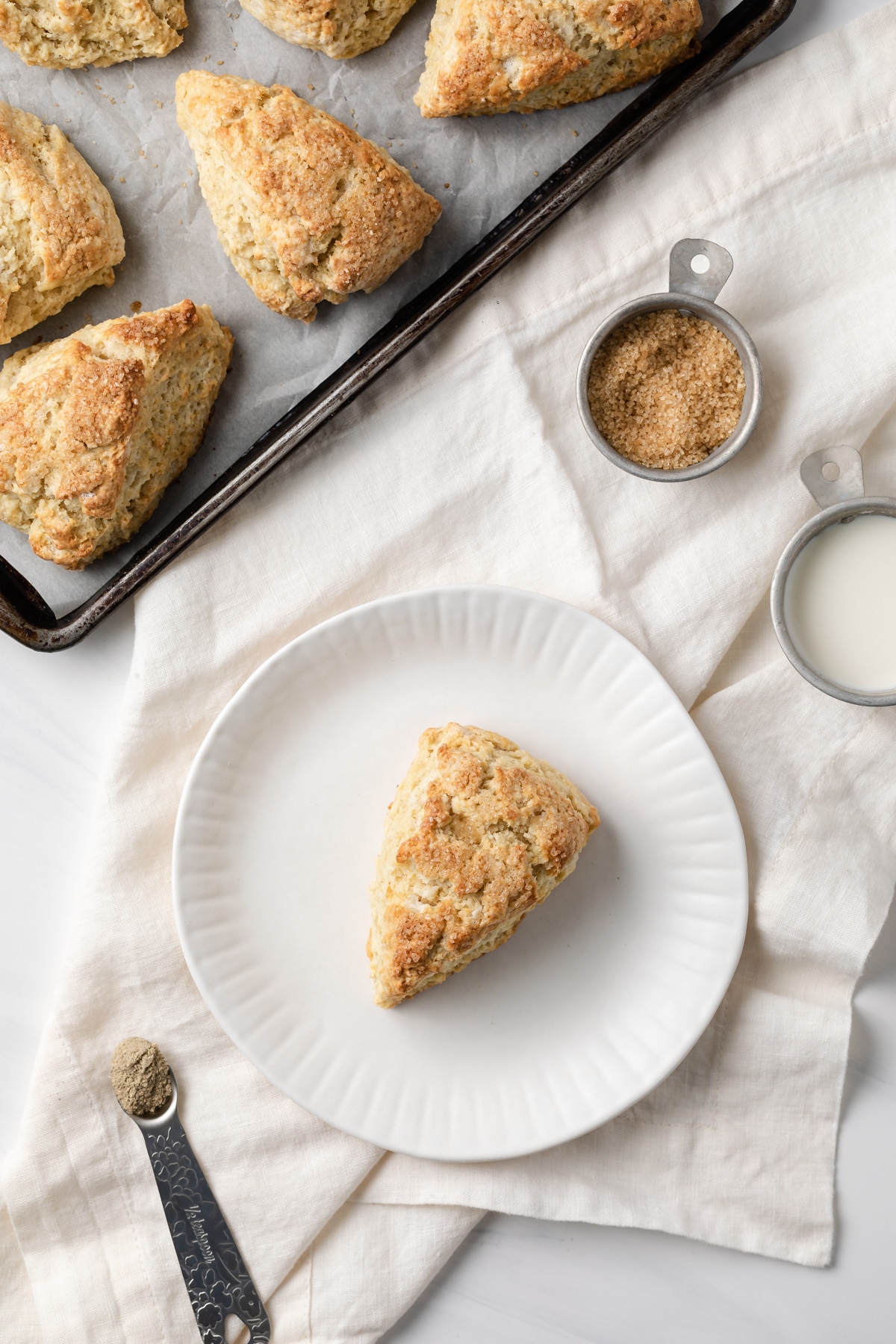 overhead view of vanilla cardamom scones on baking sheet and one on white plate