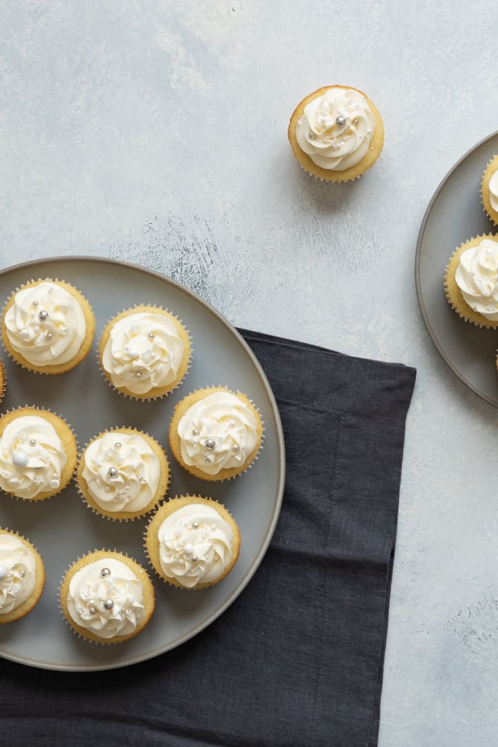 several vanilla cupcakes on a gray plate with a blue napkin underneath