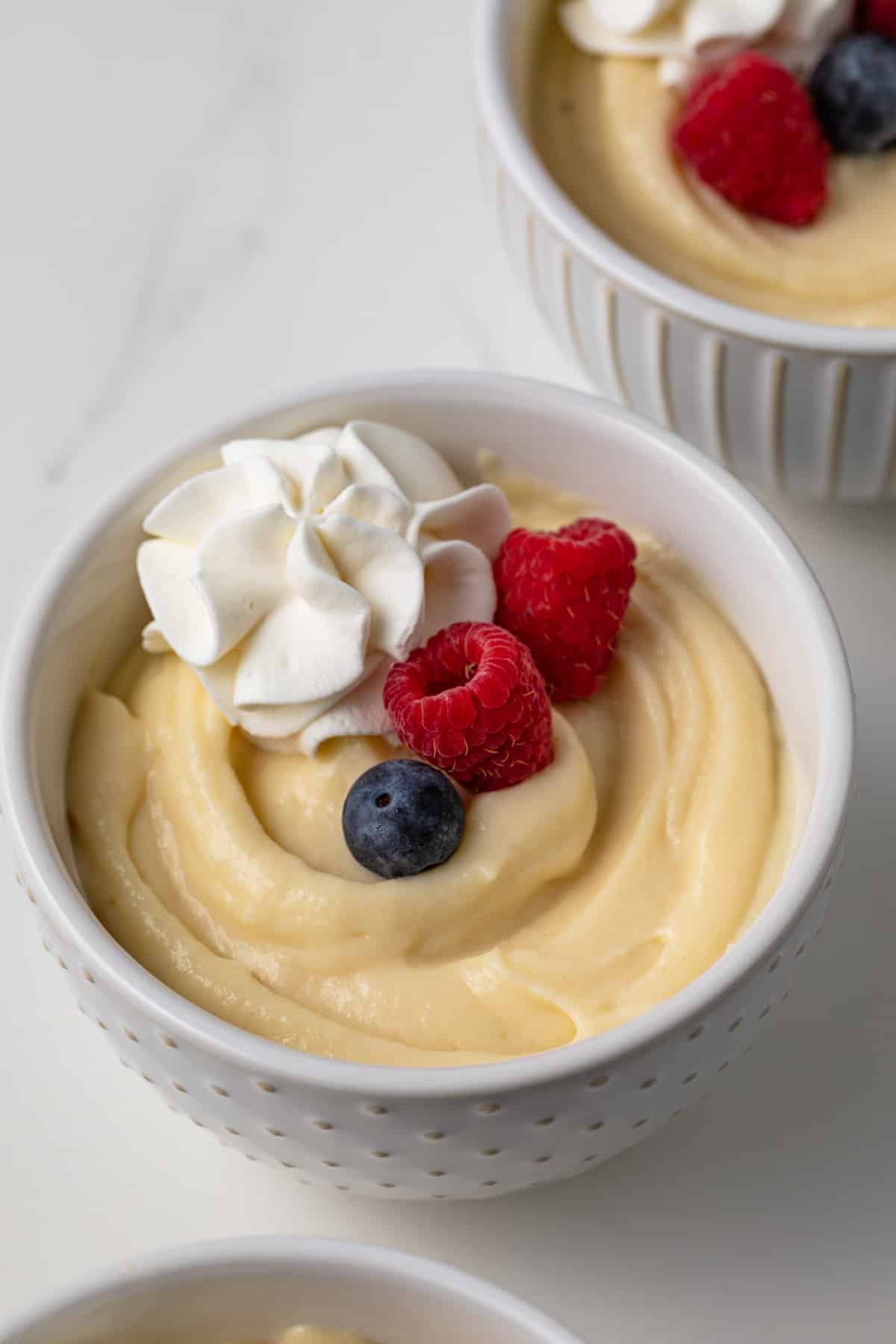 Vanilla pudding in white bowl with whipped cream and berries.