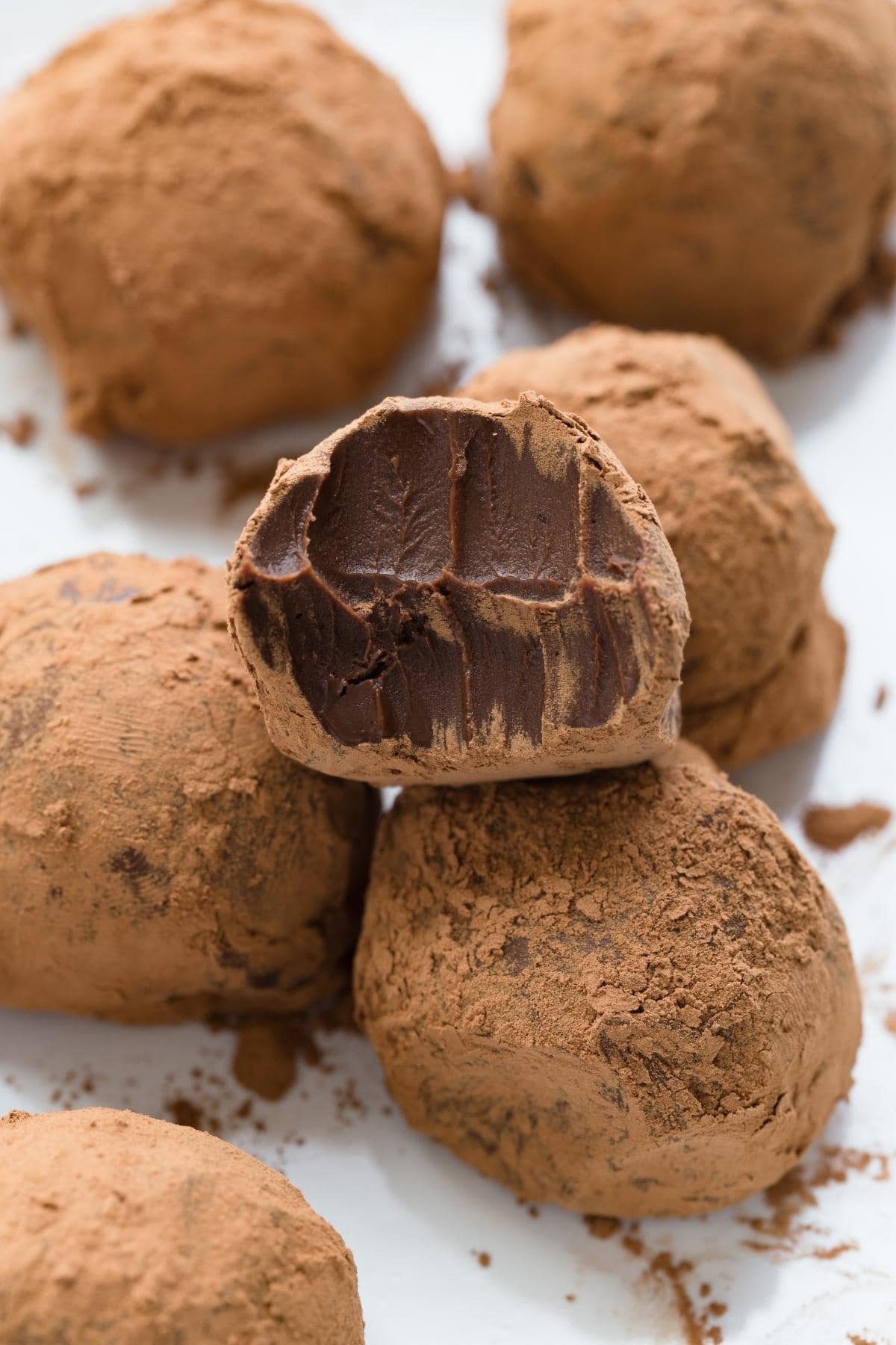 Vegan chocolate truffles on a white plate with a bite taken out of one of the truffles.