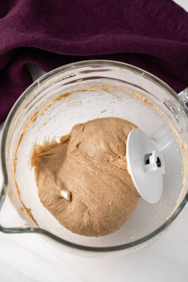 Dough wrapped around a dough hook in a glass mixing bowl