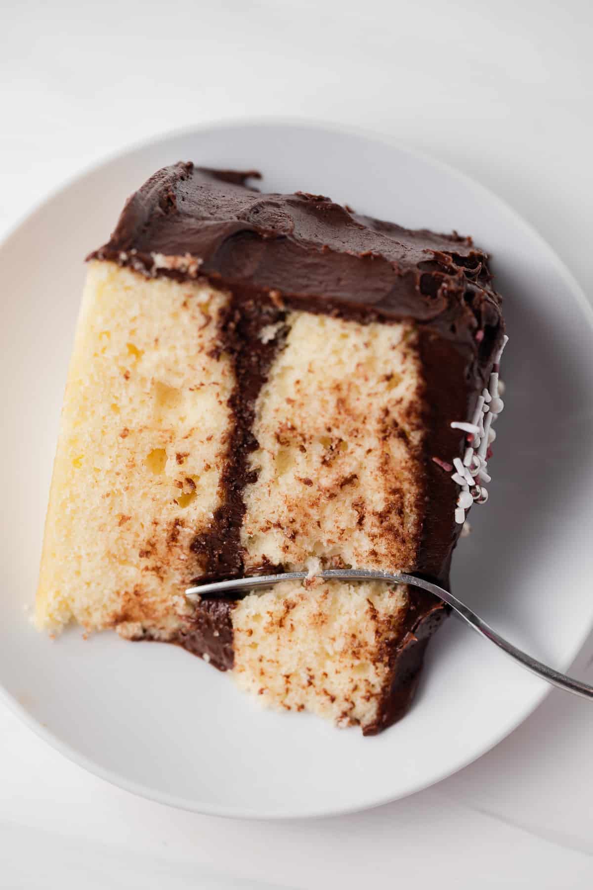 Fork taking out a bite of yellow cake on white plate.