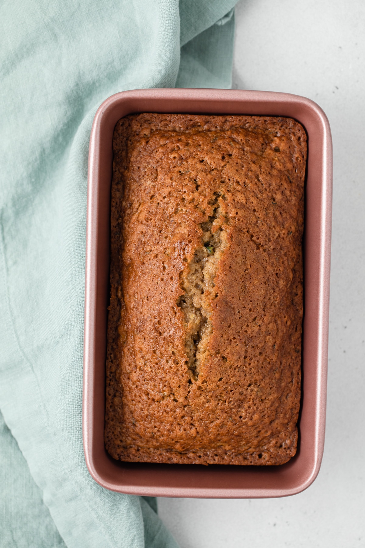 overhead of zucchini bread in pink loaf pan with pale blue napkin